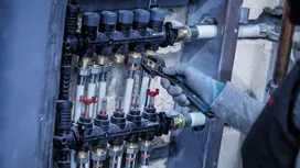 Person wearing safety equipment adjusts a plumbing manifold with a wrench.