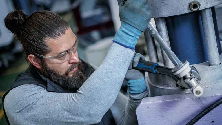 Person wearing safety equipment tightens a large bolt on industrial machinery.