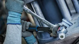 Person wearing safety equipment tightens a pipe joint with two wrenches.