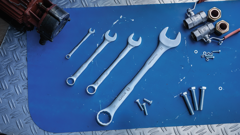 Four open-end wrenches with bolts and metal parts arranged on a blue work surface.