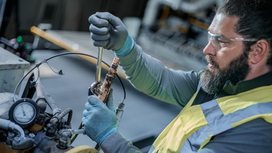 Person wearing safety equipment tightens a fitting on industrial machinery.