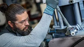 A person wearing safety equipment tightens a large bolt with a wrench on industrial machinery.
