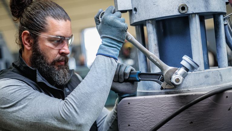 Person wearing safety equipment uses a wrench to tighten a large industrial machine.