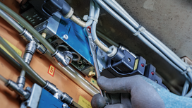 Person wearing safety equipment tightens a pipe fitting on electrical equipment.