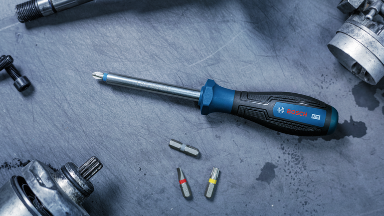 Screwdriver with interchangeable bits on a metal work surface.