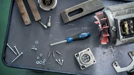 Screwdriver and assorted bolts, washers, and machine parts scattered on a workbench.