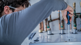 Person wearing safety equipment tightens a screw on a metal panel.