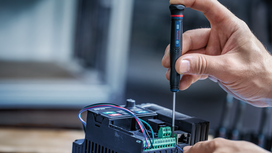 Person uses a screwdriver to adjust wiring on an electronic device.