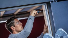 Person wearing safety equipment tightens a screw in a door frame.