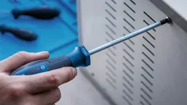 Person uses a screwdriver to fasten a screw on a metal panel.