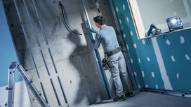A person wearing safety equipment checks wall alignment at a construction site.