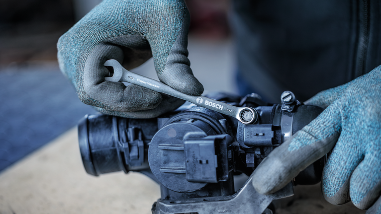 Person wearing safety equipment tightens a bolt on machinery with a wrench.