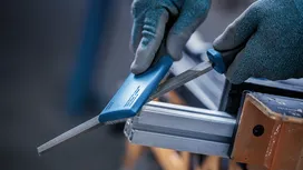 Person wearing safety equipment uses a file to smooth a metal bar.