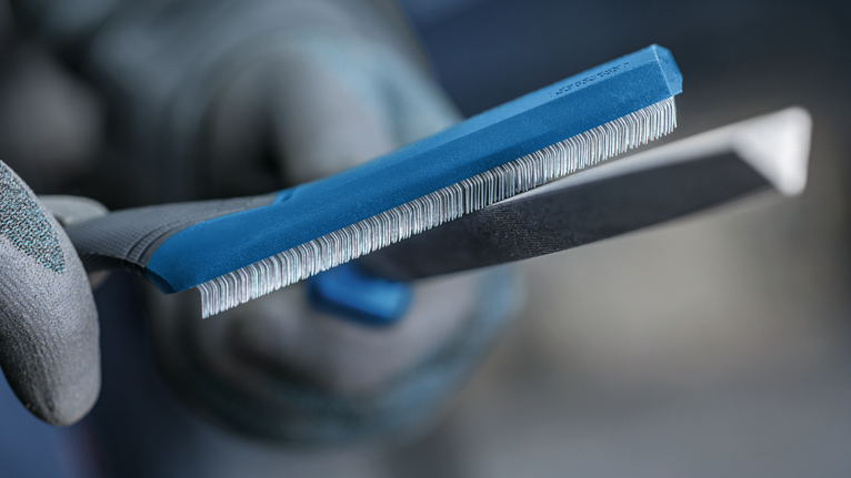 Person wearing safety equipment holds a sharpening file close to a metal tool edge.
