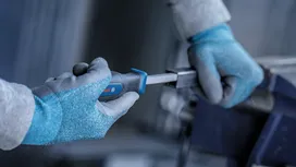 Person wearing safety equipment tightens a metal piece with a screwdriver.