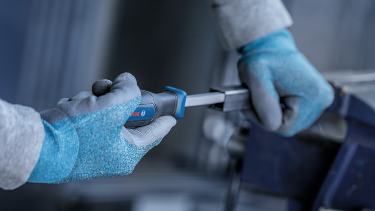 Person wearing safety equipment tightens a metal piece with a screwdriver.