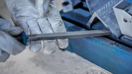 Person wearing safety equipment filing the edge of a metal piece.