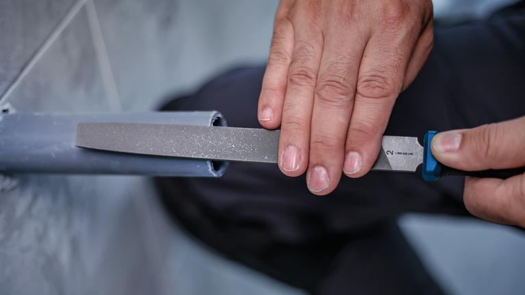 Person files the edge of a plastic pipe before installation.