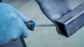 Person wearing safety equipment files the edge of a metal pipe.