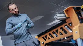 Person wearing safety equipment tightens a tool near a metal workbench.