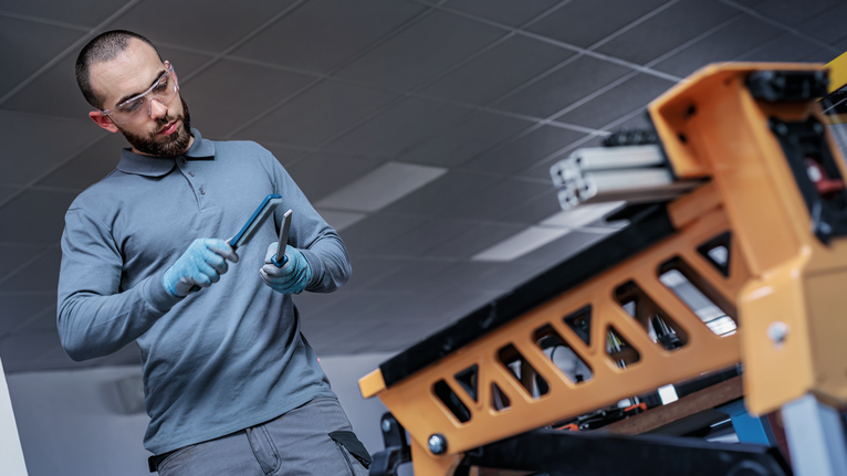Person wearing safety equipment tightens a tool near a metal workbench.