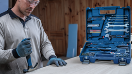 Person wearing safety equipment uses a hammer next to an open toolkit on a table.