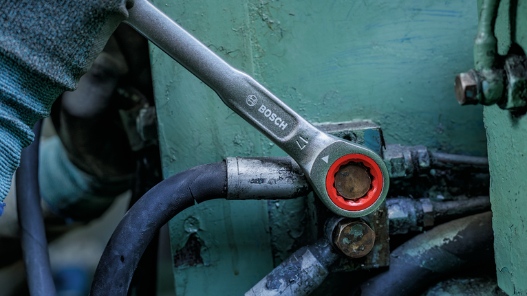 Person wearing safety equipment tightens a bolt with a ratcheting wrench.