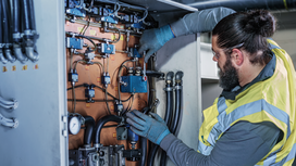 Person wearing safety equipment repairs wiring inside an industrial electrical panel.