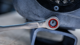 A ratchet wrench tightens a bolt on a metal machine housing.