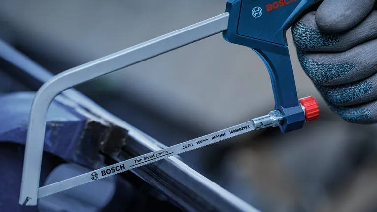 Person wearing safety equipment uses a metal hand saw to cut a pipe.