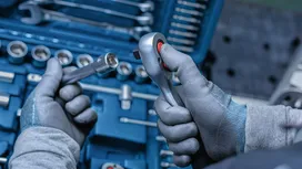 Person wearing safety equipment holds a ratchet near a socket set.