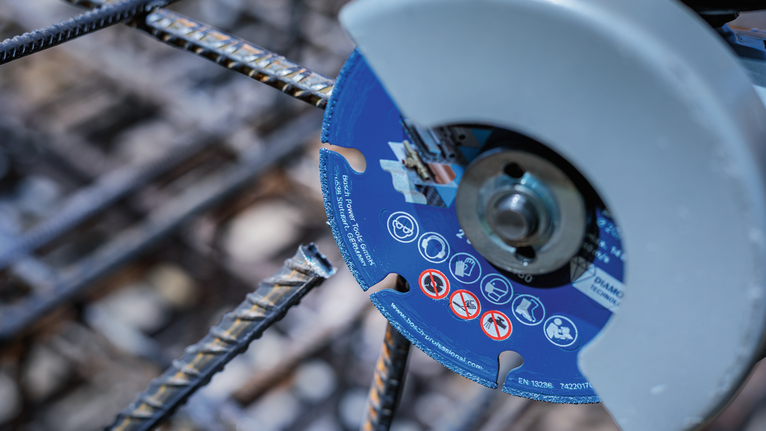 A diamond cutting wheel slices through a steel rebar at a construction site.