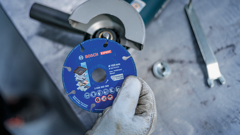 Person wearing safety equipment holds a blue diamond cutting disc near an angle grinder.
