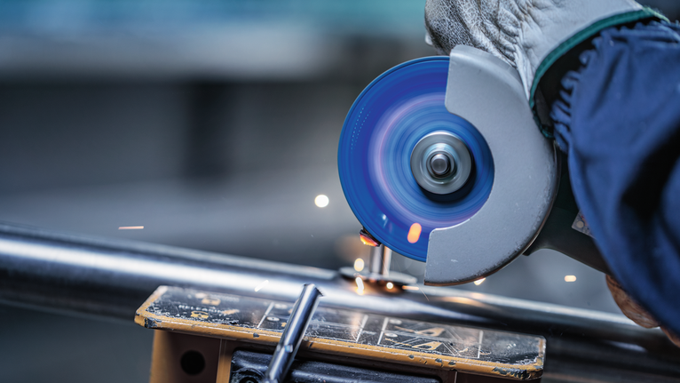 Person wearing safety equipment cuts a metal pipe with an angle grinder.