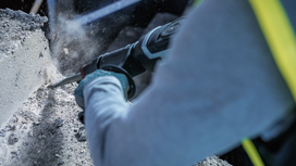 Person wearing safety equipment demolishes concrete with a reciprocating saw.