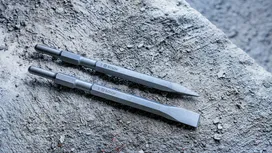 Two chisel drill bits lying on a rough concrete surface.