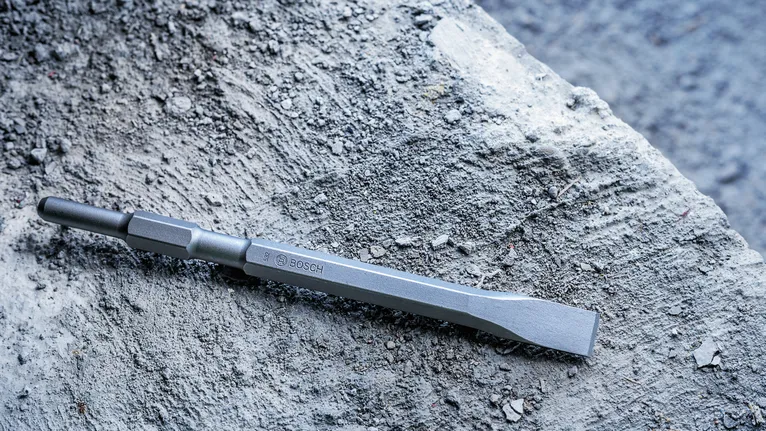 Flat chisel resting on rough concrete surface.