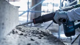 Person wearing safety equipment demolishes concrete with a rotary hammer.