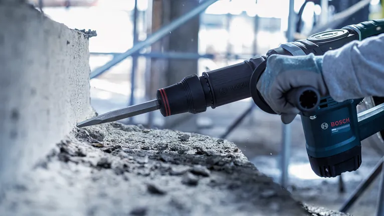 Person wearing safety equipment demolishes concrete with a rotary hammer.