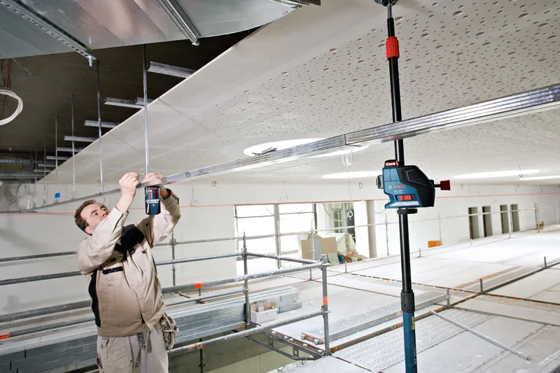 LR 7 A person wearing safety equipment aligns ceiling framework using a laser leveling tool.