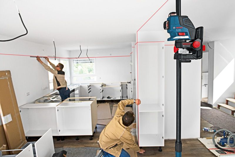 Two persons installing cabinets align shelves using a laser leveling tool.