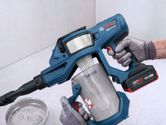 A person wearing safety equipment empties dust from a cordless dry vacuum cleaner.
