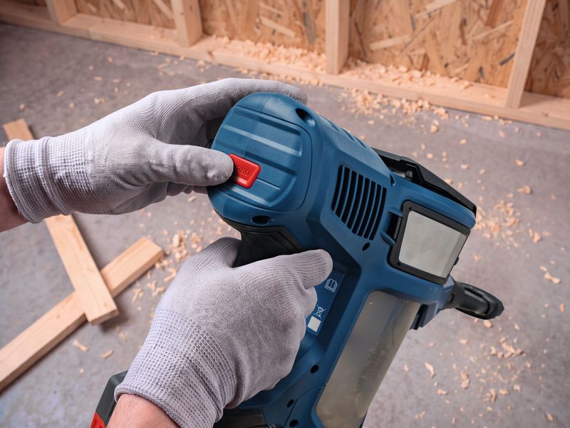 A person wearing safety equipment holds a cordless dry vacuum cleaner at a construction site.