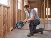 A person wearing safety equipment uses a cordless dry vacuum cleaner on a construction site.