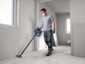 A person wearing safety equipment cleans a construction site floor with a cordless dry vacuum cleaner.