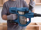 A person wearing safety equipment holds a cordless dry vacuum cleaner.