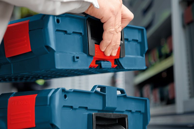 A person stacks blue plastic toolboxes with red latches in a storage area.