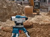 Laser leveling tool on a tripod at a construction site near an excavator.