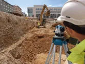 Person wearing safety equipment uses a surveyor level at a construction excavation site.