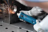 A person wearing safety equipment grinds a metal edge with an electric tool, creating sparks.